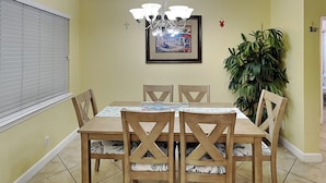 A dining area with a table and chairs, a chandelier, a framed picture, and a potted plant.