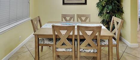 Un coin repas comprenant une table et des chaises, un lustre, un tableau encadré et une plante en pot.