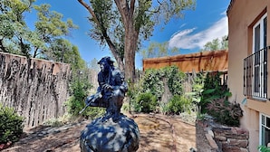 A statue of a seated figure on a sphere in a garden with a wooden fence, trees, and a building with a balcony. - Casa en Canyon by Kokopelli Property Management (Santa Fe)