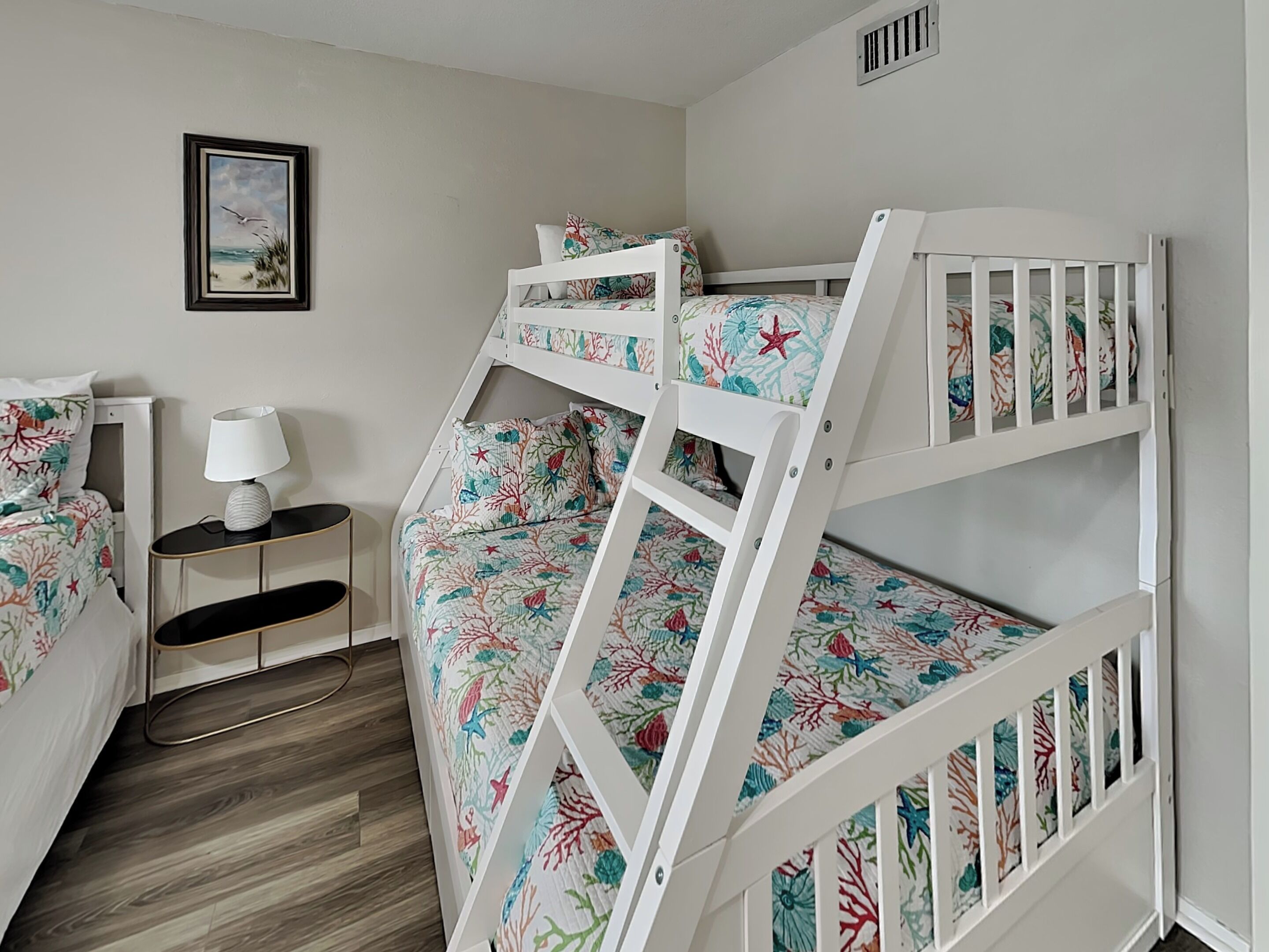 A bunk bed room with a nightstand, a lamp, and a framed picture on the wall.