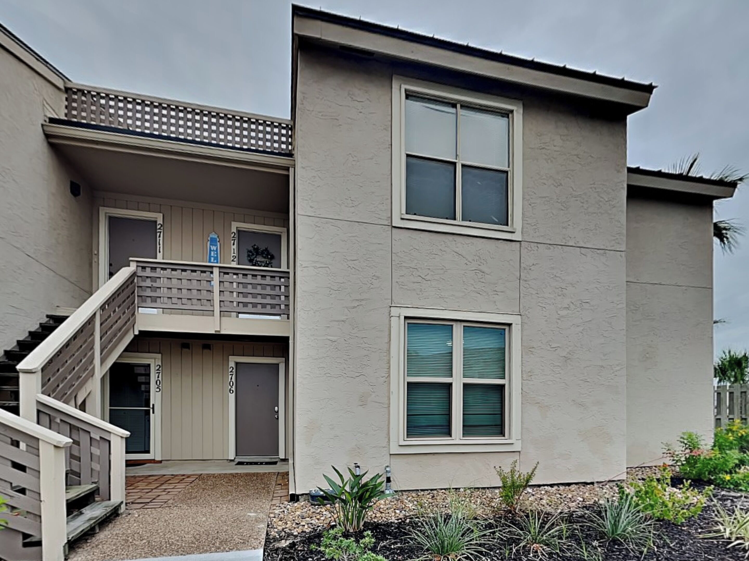 Une maison à deux étages avec un balcon, une porte d’entrée et un petit jardin.