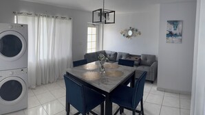 Un salon moderne comprenant un canapé, une table à manger avec des chaises, un lave-linge et un luminaire suspendu au plafond.