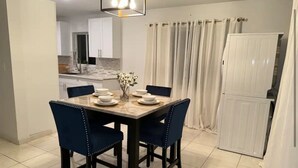 Un coin repas avec une table dressée pour quatre personnes, deux chaises bleues, un vase avec des fleurs et, au fond, un meuble blanc.