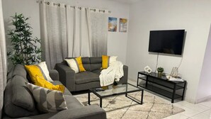 Un salon moderne avec deux canapés gris, une table basse en verre, un meuble TV noir et une grande plante.