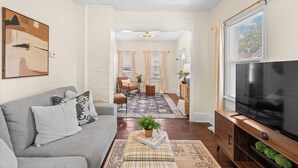 A living room with a grey sofa, a flat-screen TV, and a wooden entertainment unit. - Charming 1-bedroom house with WiFi, AC in peaceful Cleveland 3215 (Cleveland)