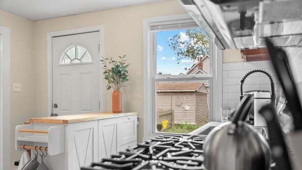 A kitchen with a gas stove, a white cabinet, a window with a view of a house, and a plant on the windowsill. - Charming 1-bedroom house with WiFi, AC in peaceful Cleveland 3215 (Cleveland)