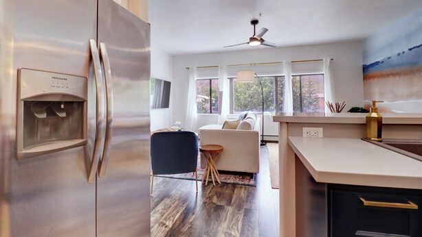 A modern kitchen with a stainless steel refrigerator, a ceiling fan, and a large window with curtains. - Fully Remodeled Mountain Condo, Silverthorne, A1 Brian (Silverthorne)