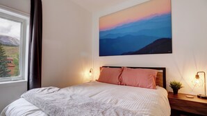 A neatly made bed with a white and gray blanket, a wooden headboard, and two pink pillows. A painting of a mountain landscape hangs above the bed. - Fully Remodeled Mountain Condo, Silverthorne, A1 Brian (Silverthorne)