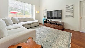 Ein geräumiges Wohnzimmer mit Ecksofa, Flachbildfernseher, Couchtisch und einem gemusterten Teppich.