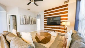 Ein modernes Wohnzimmer mit einer Couch, einem Couchtisch und einem Flachbildfernseher, der an einer Wand aus Holzpaneelen angebracht ist.