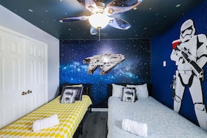 Une chambre avec une fresque représentant un vaisseau spatial, un ventilateur de plafond et une figurine de Stormtrooper.
