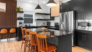 Una cocina moderna con una isla central, armarios negros, electrodomésticos de acero inoxidable y sillas de madera.