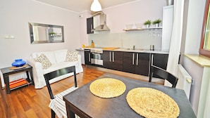 A compact living space with a kitchenette, a dining area with a table and woven placemats, a sofa with patterned cushions, and a mirror on the wall. - Duet by Grand Apartments (Sopot)