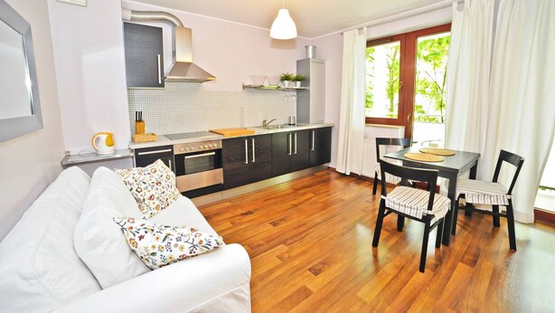 A compact kitchen with modern appliances, a dining area with a table and chairs, and a sofa with floral cushions. - Duet by Grand Apartments (Sopot)