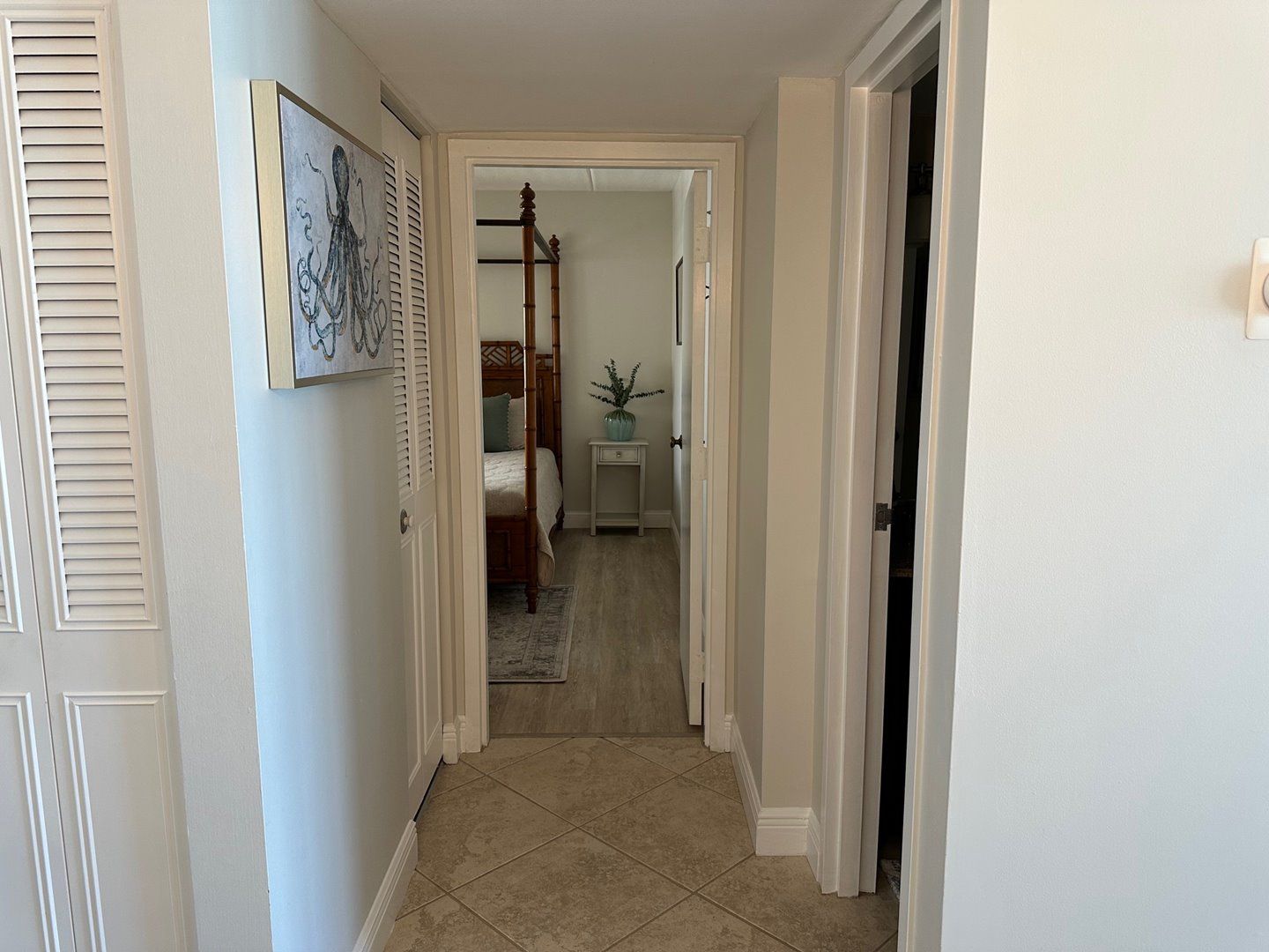 Un pasillo con una cama, una mesita de noche y una puerta que da a otra habitación.