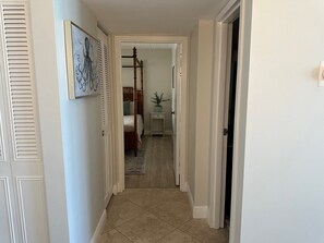 Un pasillo con una cama, una mesita de noche y una puerta que da a otra habitación.