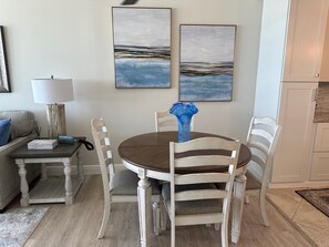 Un comedor con una mesa redonda, sillas blancas, un jarrón azul y dos cuadros abstractos en la pared.