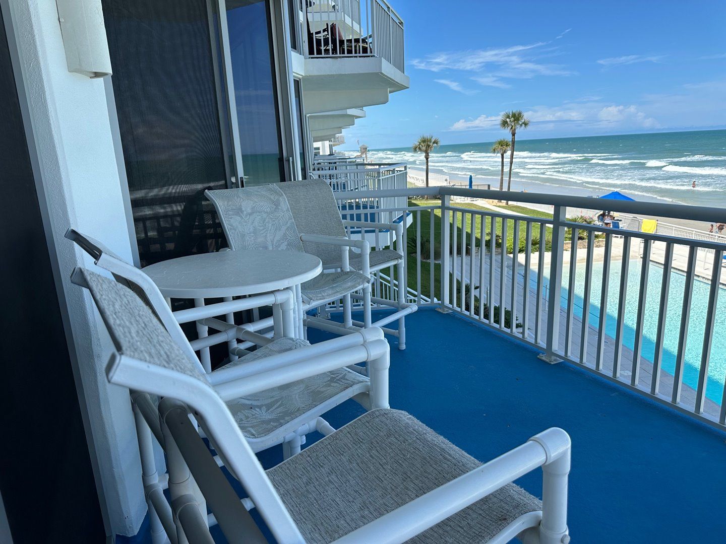 A balcony with white wicker furniture, a pool, and a view of the ocean.
