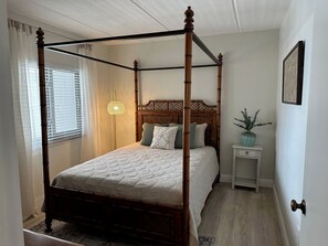 Uma cama de dossel com cabeceira de madeira, uma mesa de cabeceira com um vaso e uma janela com persianas.