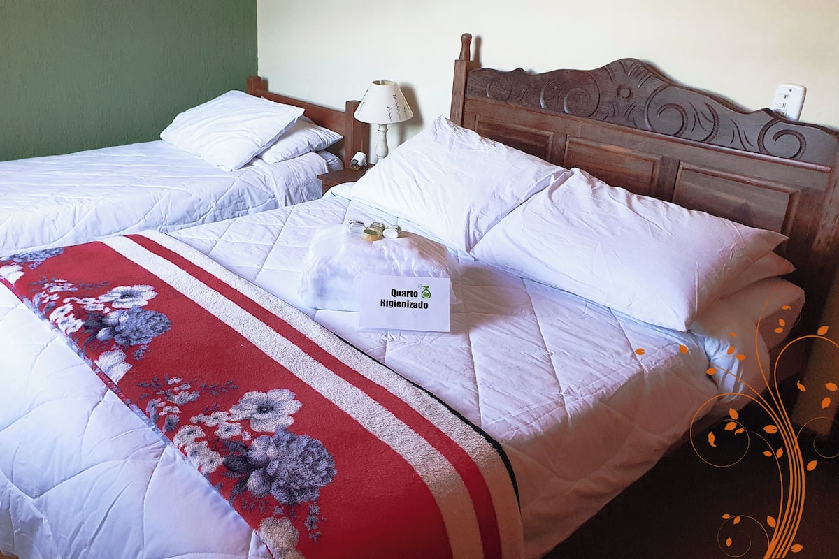 Two single beds with white bedding and a red floral bedspread, a wooden headboard, and a bedside table with a lamp.