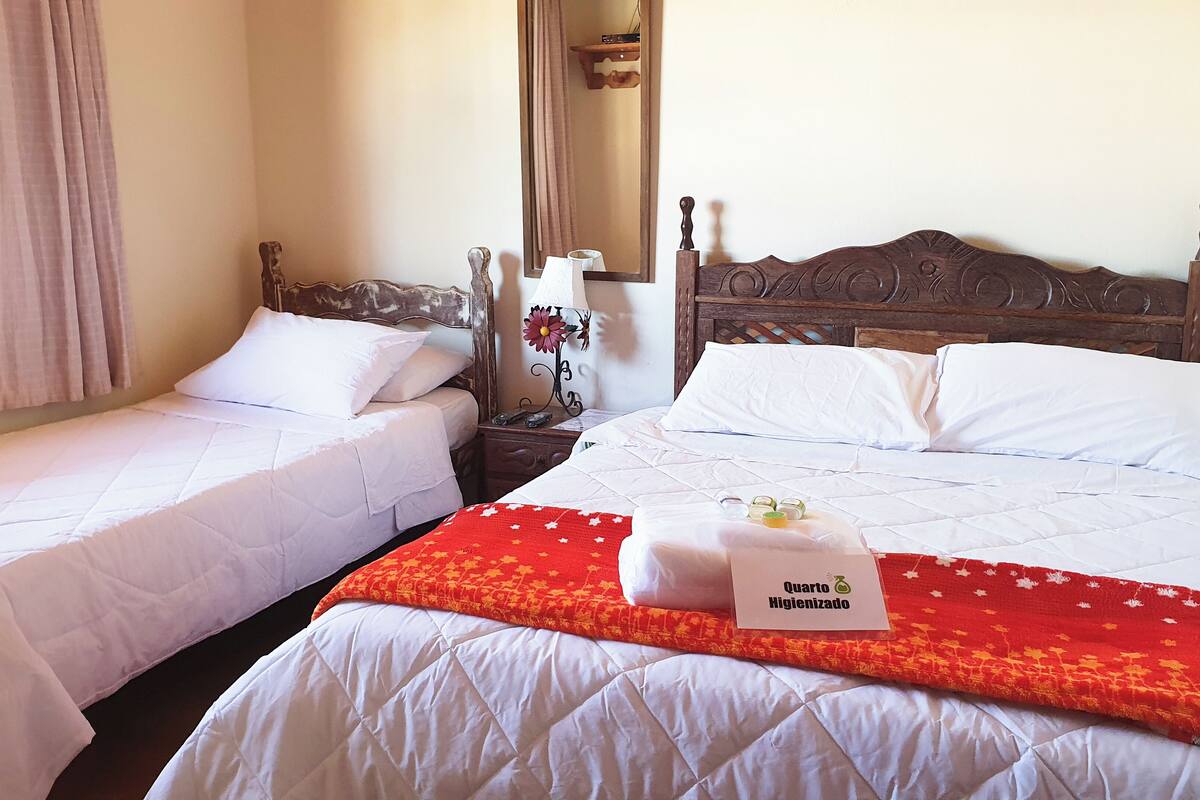 A hotel room with two single beds, a wooden headboard, a nightstand with a lamp, and a red blanket with a towel.