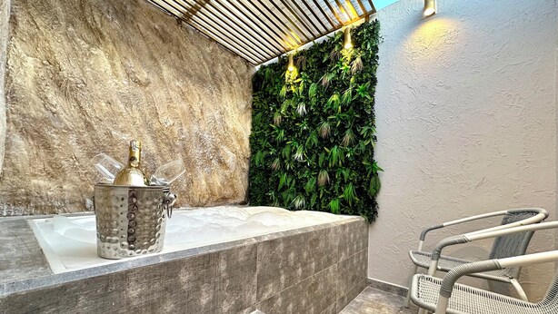 A bathroom with a stone wall, a green wall with plants, a bathtub, and a chair. - HOTEL PARIS CARRE (Valledupar)