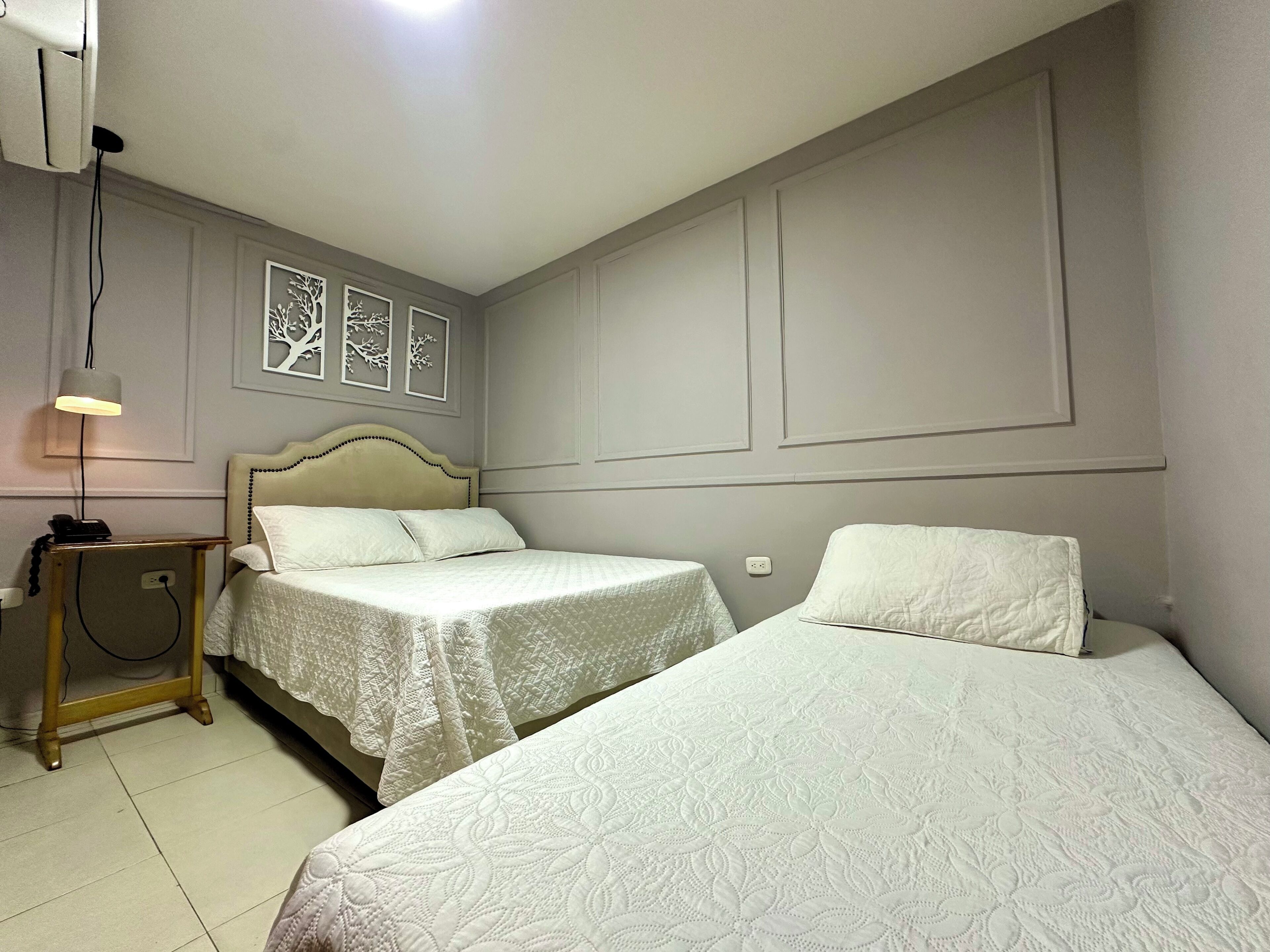 A hotel room with two beds, a bedside table with a lamp, and a wall-mounted telephone.