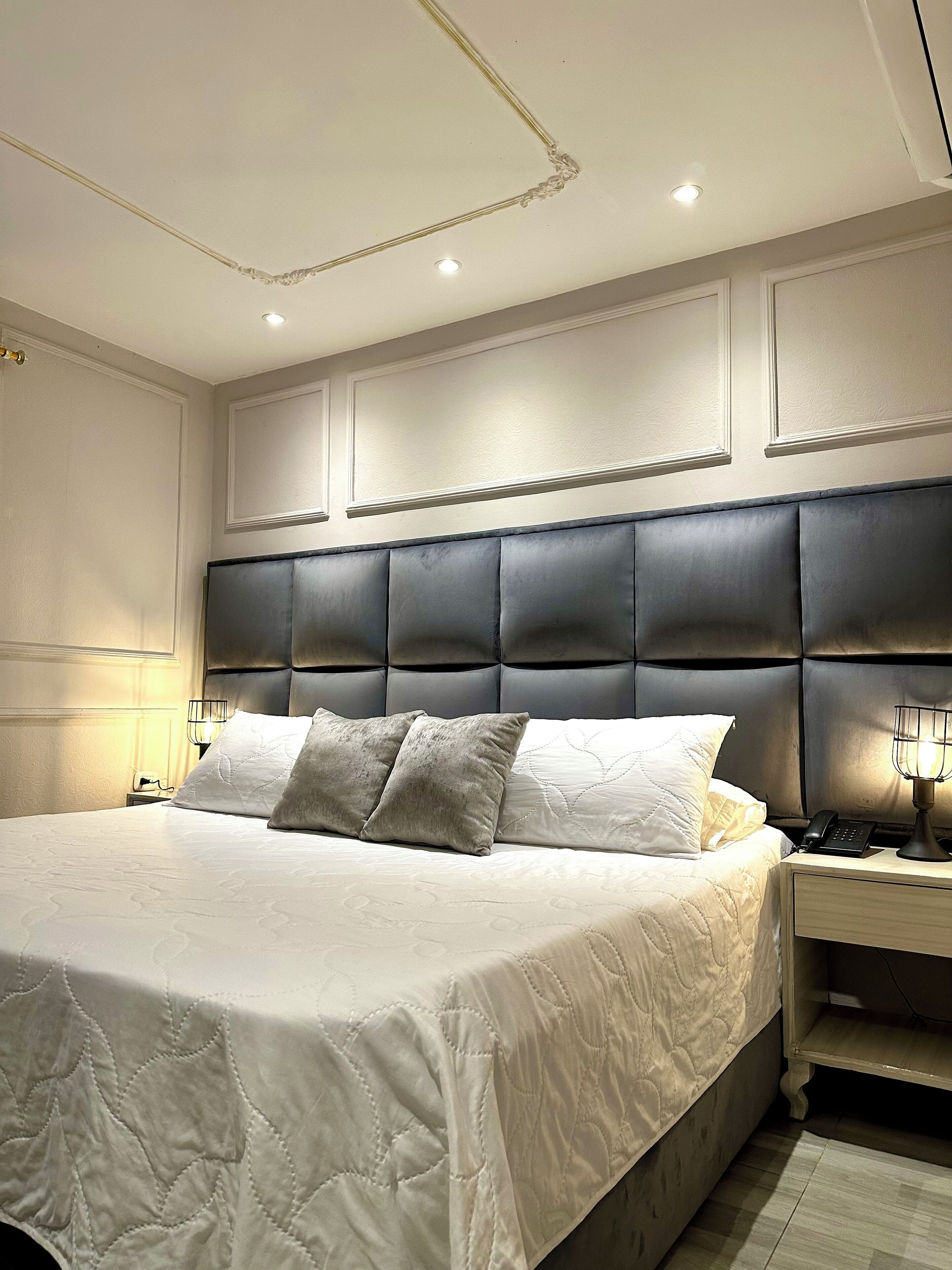 A large bed with a tufted headboard, two bedside lamps, and a nightstand with a phone.