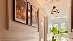 A hallway with framed pictures, a large potted plant, and a hanging light fixture. - HOTEL PARIS CARRE (Valledupar)