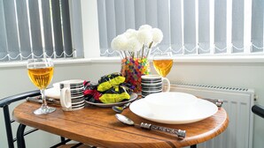 A dining table set with plates, a glass of wine, a vase with flowers, and a colorful mug. - Central twin bed flat (Cardiff)