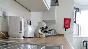 A kitchen with a Prolex coffee maker, a kettle, and a toaster. There is a fire safety sign on the wall and a window with blinds. - Central twin bed flat (Cardiff)