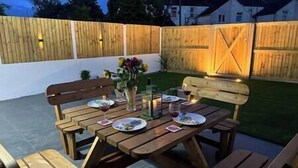 An outdoor patio with wooden benches and tables, a vase with flowers, and a candle. - Central twin bed flat (Cardiff)