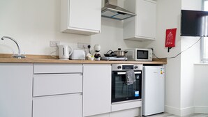 A compact kitchen with white cabinets, a microwave, a toaster, and a small oven. - Central twin bed flat (Cardiff)