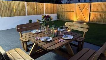 An outdoor patio with wooden benches and tables, a vase with flowers, and a candle.