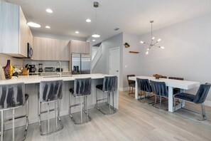 Cocina moderna con una isla central, taburetes de bar y un comedor con mesa blanca y sillas oscuras.