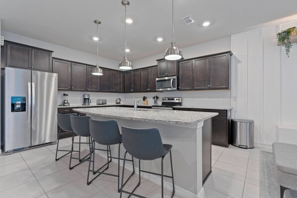 A modern kitchen with dark cabinets, stainless steel appliances, and a central island with bar stools.