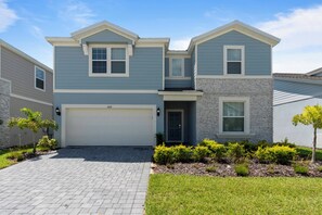A two-story house with a garage, a stone accent wall, and a small front yard with shrubs and a young tree.