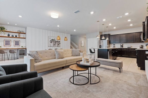 A modern living room with a sofa, coffee table, and chairs. There is a kitchen area with cabinets and appliances.