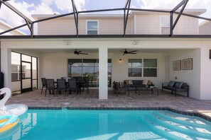 Piscina exterior cubierta con asientos y ventiladores de techo, rodeada por un patio con vistas a un edificio residencial.