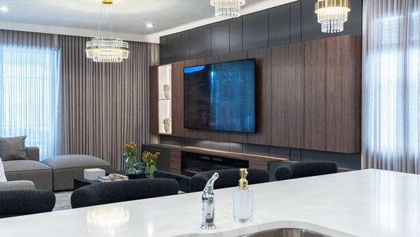 A modern living room with a large TV, a central island with a sink, dark wood paneling, and a chandelier.