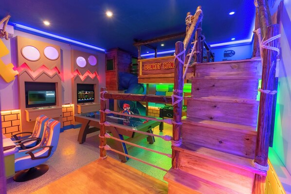 Un espacio de juegos con una estructura de madera para escalar, un tobogán y una zona de estar con mesa y sillas.
