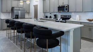 A modern kitchen with grey cabinets, stainless steel appliances, a central island with bar stools, and pendant lighting.