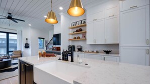 Een moderne keuken met witte kasten, een groot eiland, hangende lampen en een zichtbare trap naar een ander niveau.