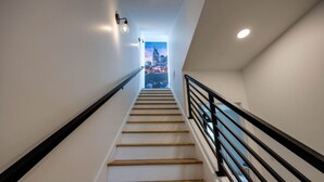 Een moderne trap met houten treden en zwarte leuningen, die uitkomt op een balkon met uitzicht op de stad.