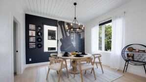 Een eetruimte met een ronde tafel, zes stoelen, een kroonluchter en een wand met ingelijste foto's en een groot abstract schilderij.