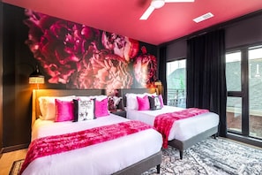 A hotel room with two beds, a large floral mural on the wall, and a cityscape view through the window.