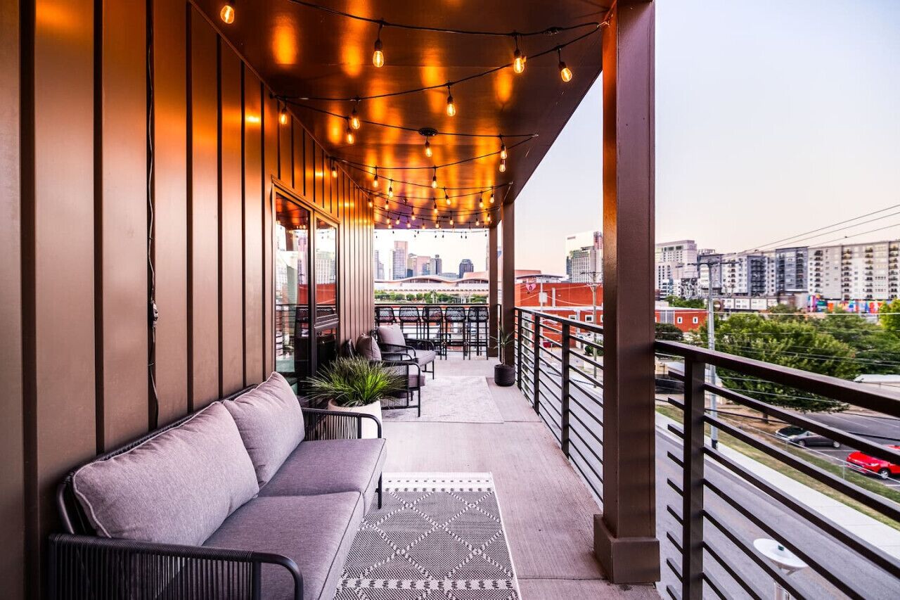 A balcony with seating, string lights, and a city view.