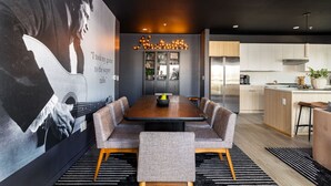 A modern dining area with a long table, cushioned chairs, and a large mural on the wall.