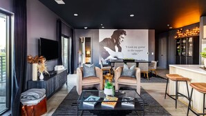 A modern living room with a flat-screen TV, two armchairs, a coffee table, and a large poster on the wall.