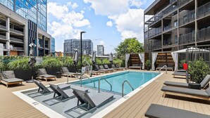 A rooftop pool area with lounge chairs, a swimming pool, and modern buildings in the background.
